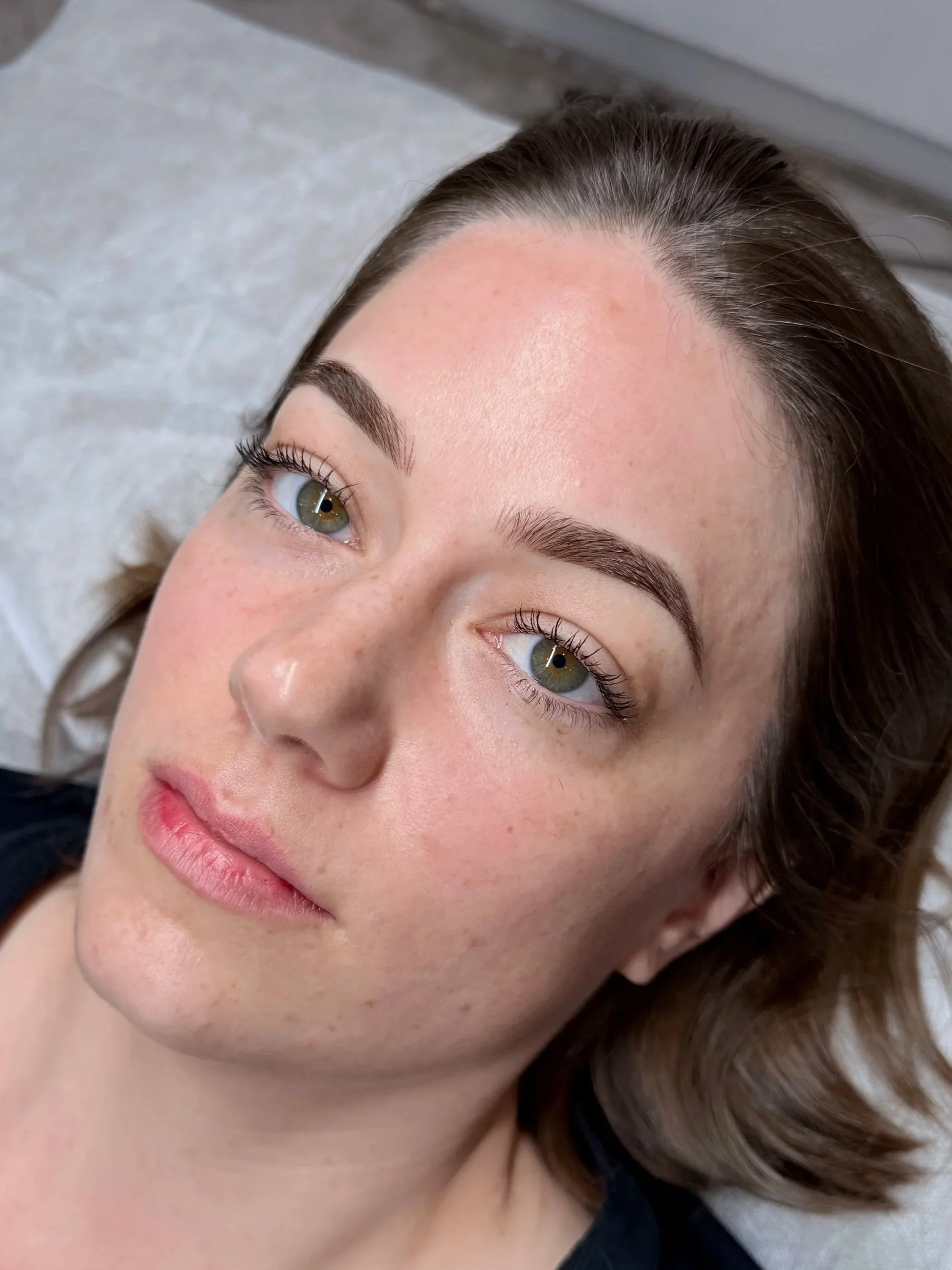 Close-up of a woman's face with light skin, green eyes, and brown hair, lying down on a gray surface.