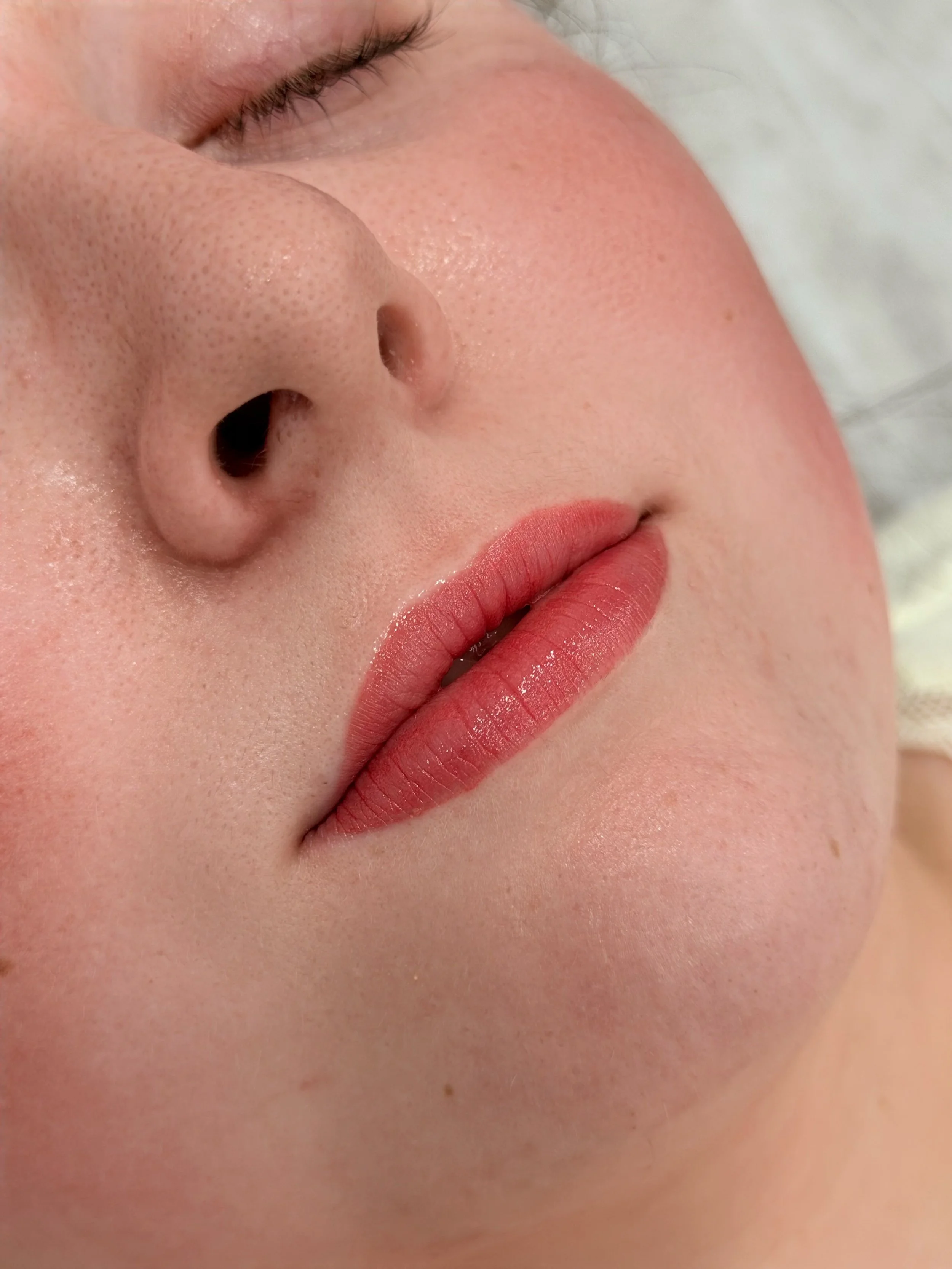 Close-up of a woman's face, showing her closed eye, nose, and lips with soft pink lipstick.