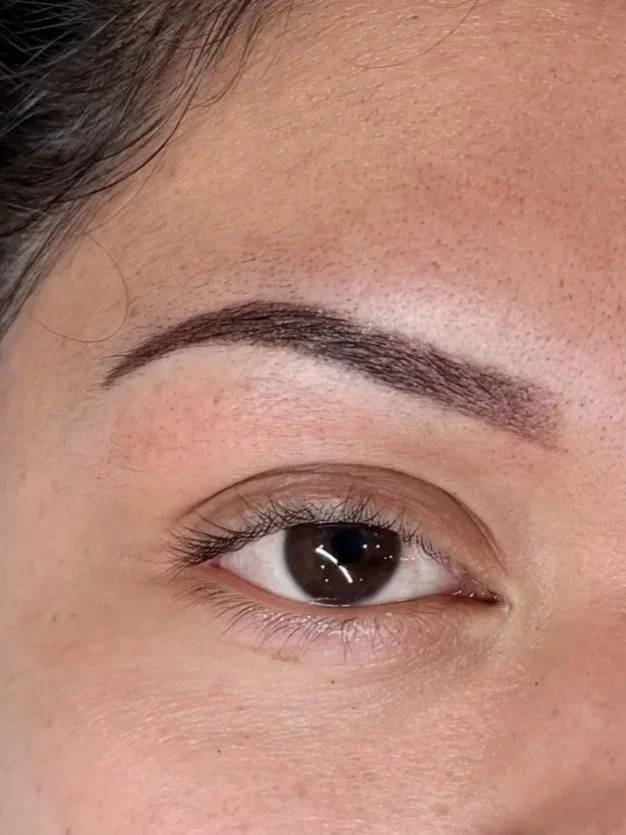 Close-up of a person's eye and eyebrow, with the eyebrow adorned with makeup or tattooing.