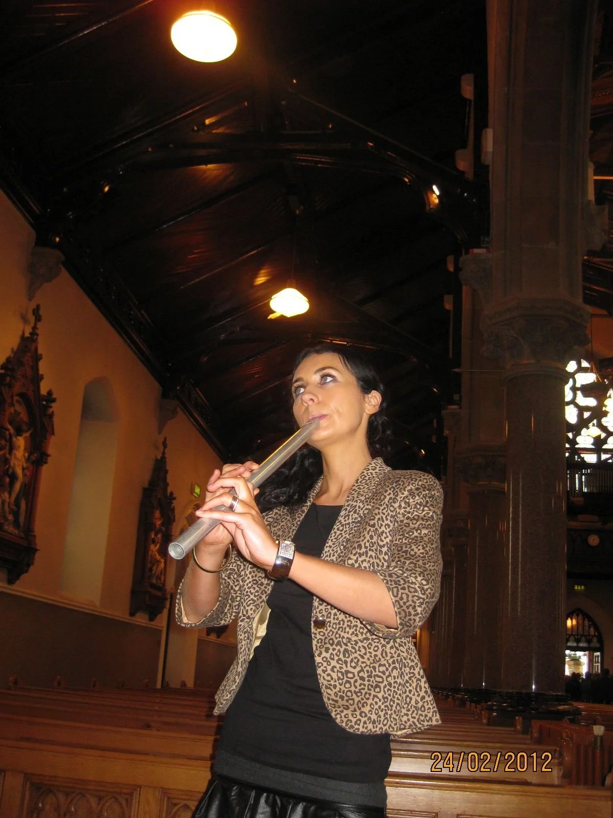 Woman playing a flute inside a church with wooden pews and ornate decorations.