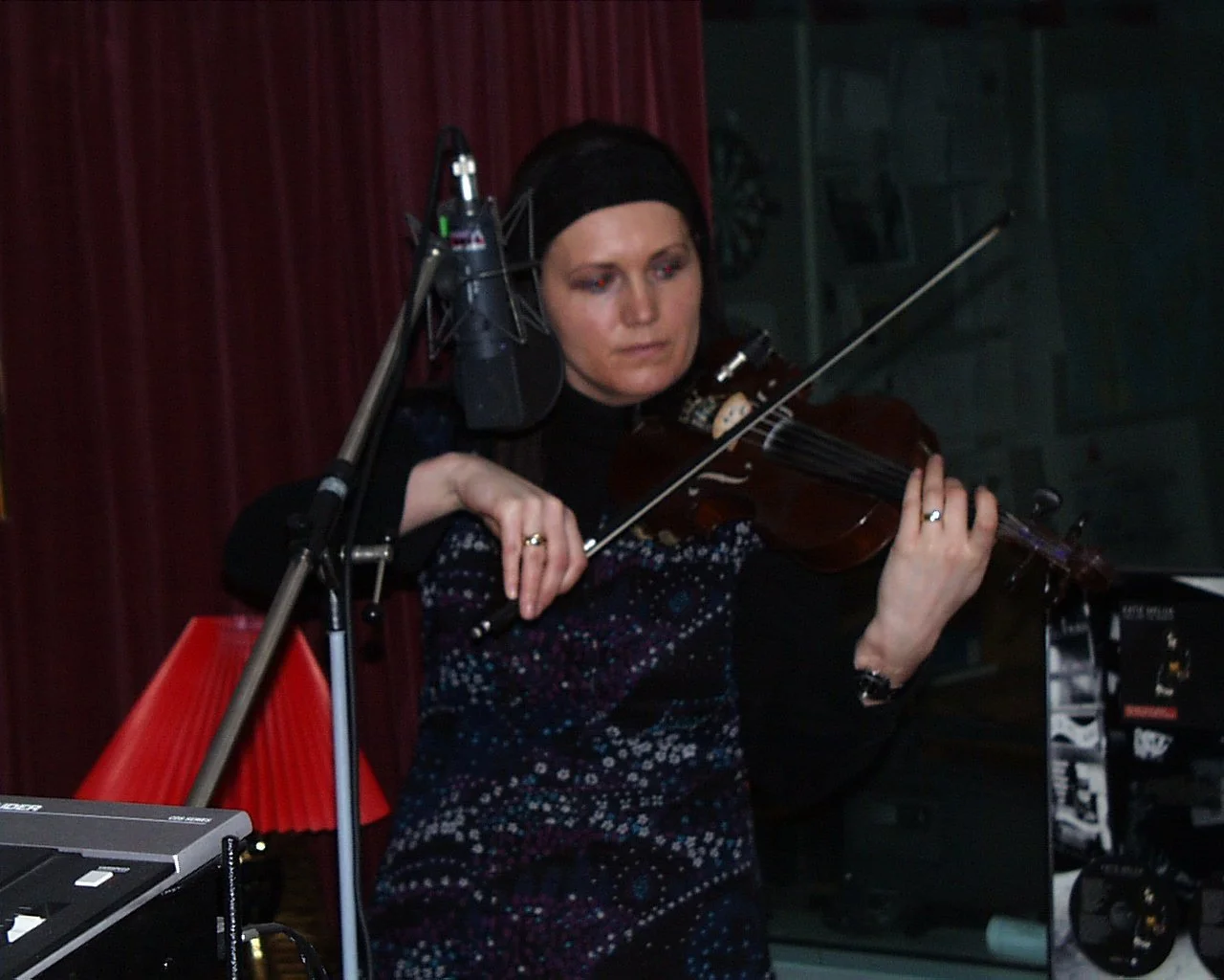 A woman wearing a black headscarf playing a violin in a recording studio with a microphone.