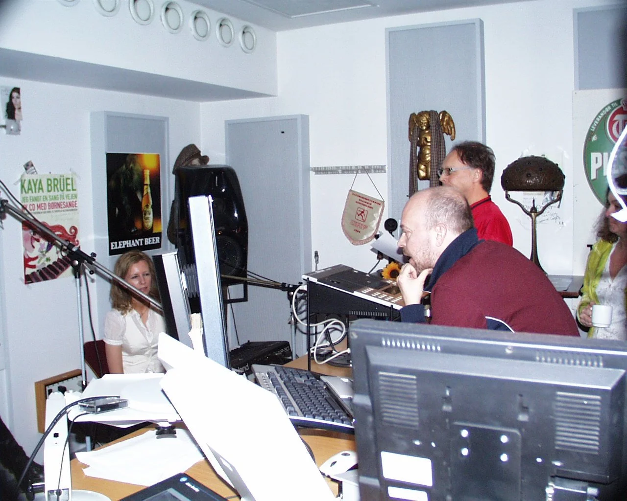 People in a recording studio with microphones, sound equipment, and posters on the wall.