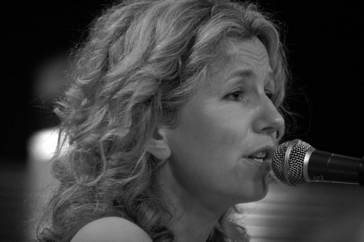 A woman with curly hair singing into a microphone.