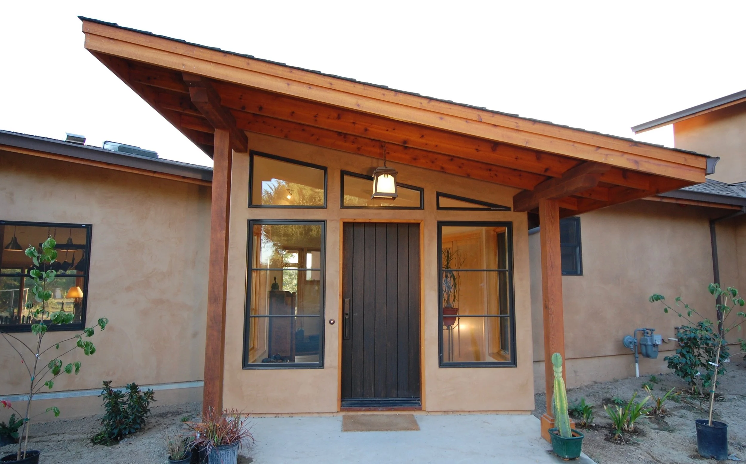 Located in Sebastopol. Front view of a house with a modern design, featuring beige stucco walls, black-framed windows, and a wooden porch with a gabled roof.