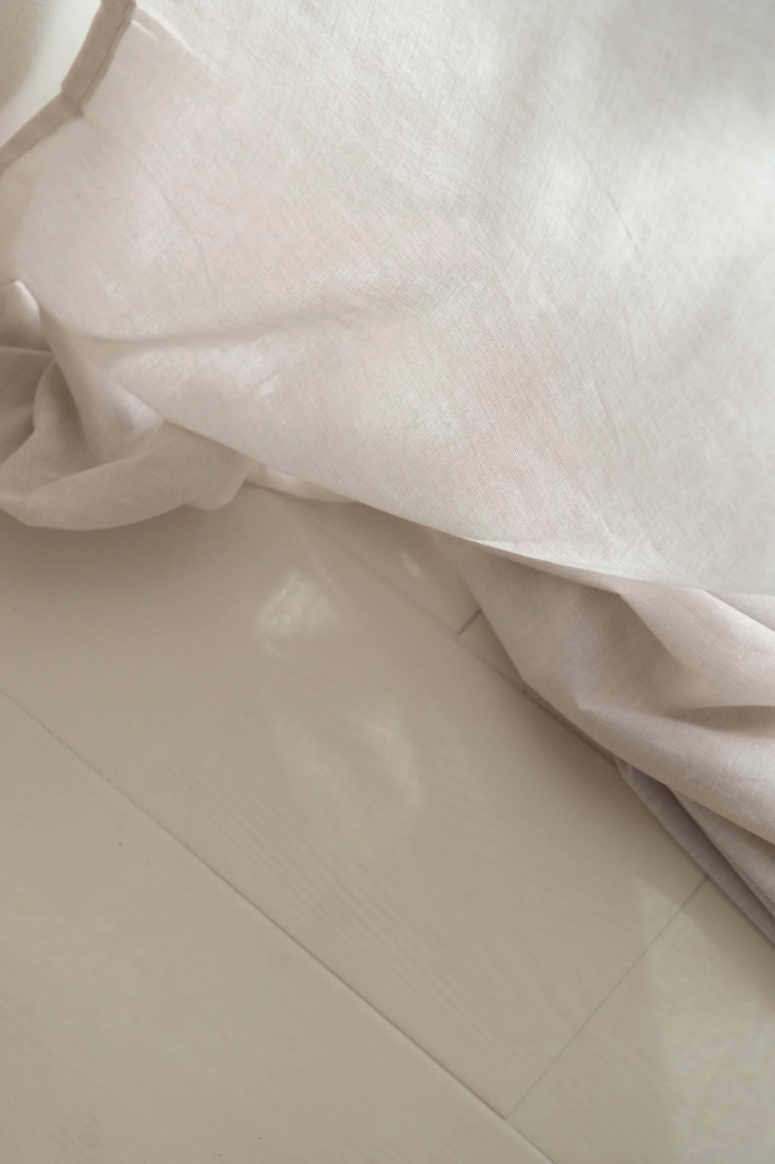 Close-up of white fabric with a knotted detail, possibly part of a curtain or bedsheet, on a white tiled floor.