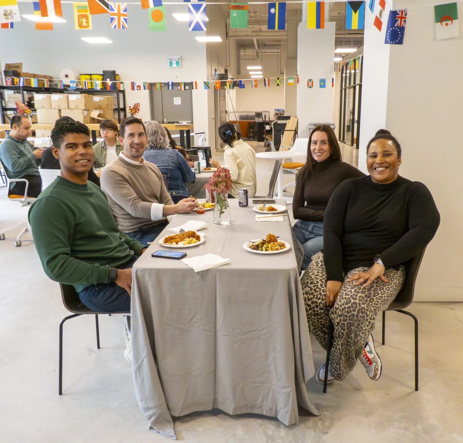 People sitting at a long table enjoying a meal in an event space decorated with international flags hanging from the ceiling.