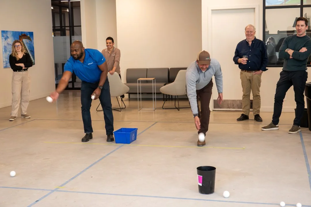 Group of people playing a game involving throwing or dropping balls into a bucket indoors.