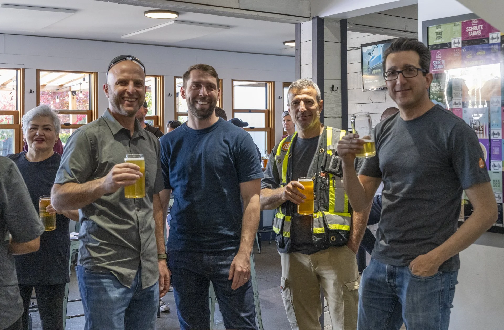 A group of five people standing indoors, enjoying drinks, with some holding glasses of beer. They are smiling and appear to be at a social gathering or celebration.