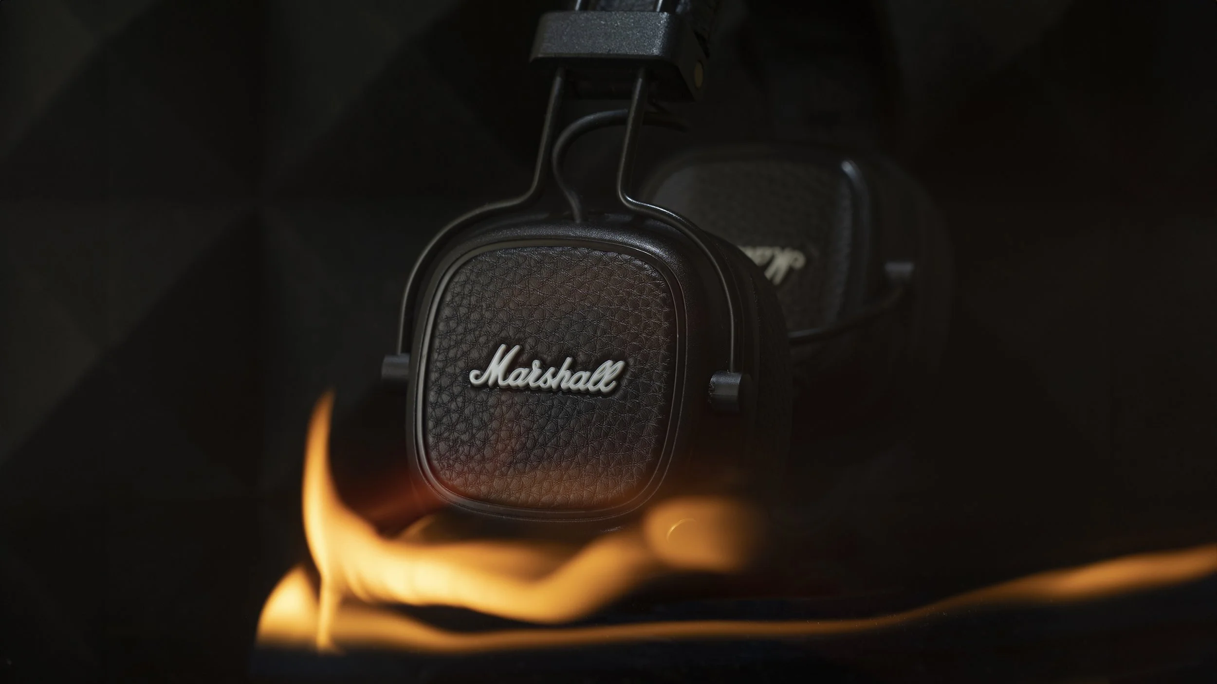 A pair of black Marshall headphones with the logo visible, resting on a surface with orange and yellow flames beneath them, dark background.
