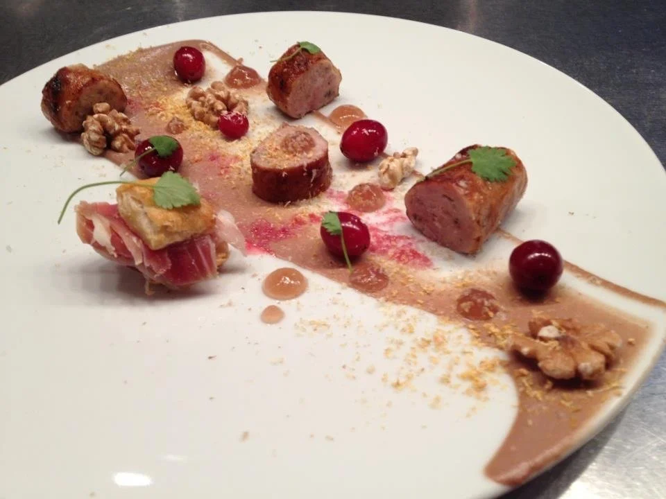 Gourmet dish with slices of sausage, cherry tomatoes, walnuts, and garnishes on a white plate.