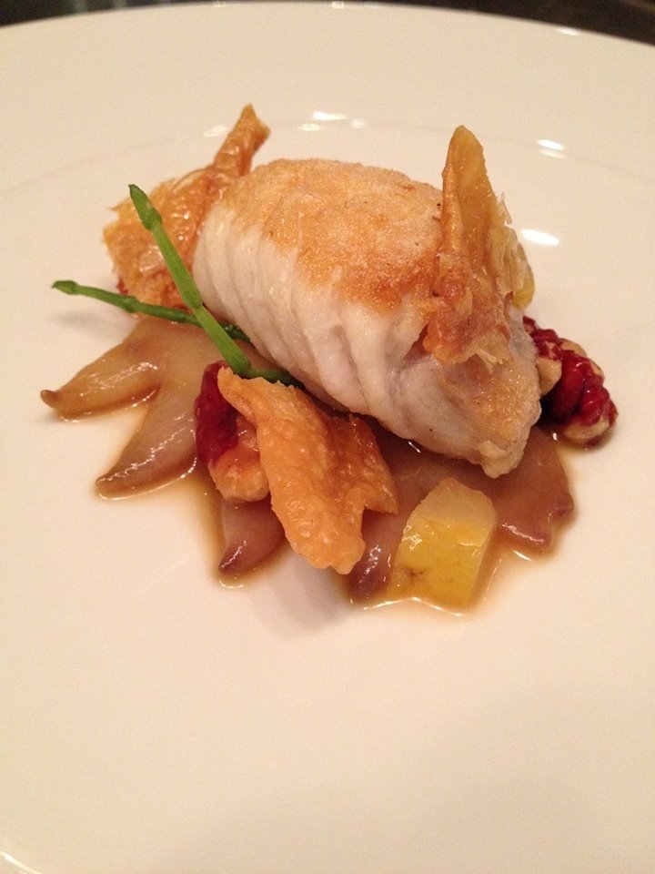 Pan-seared fish fillet with crispy skin, served with sautéed mushrooms, potatoes, and a green garnish.