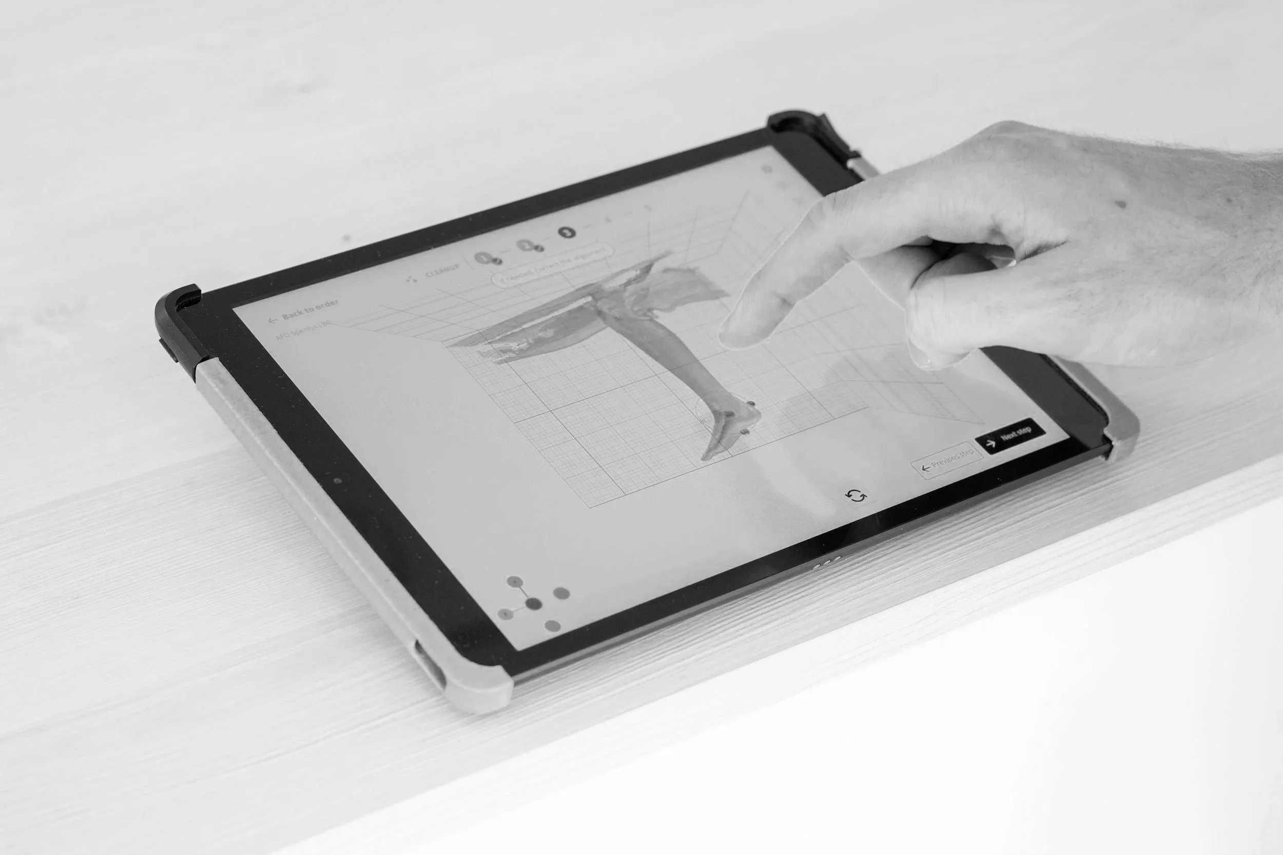 A person using a tablet to view a 3D model of a dinosaur's leg with measurement grid in a design app.