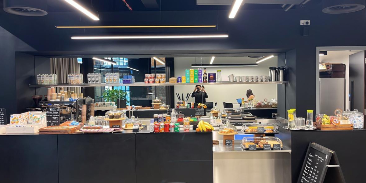 Coffee and snack station in a modern cafe with various food items, beverages, and a barista preparing drinks.