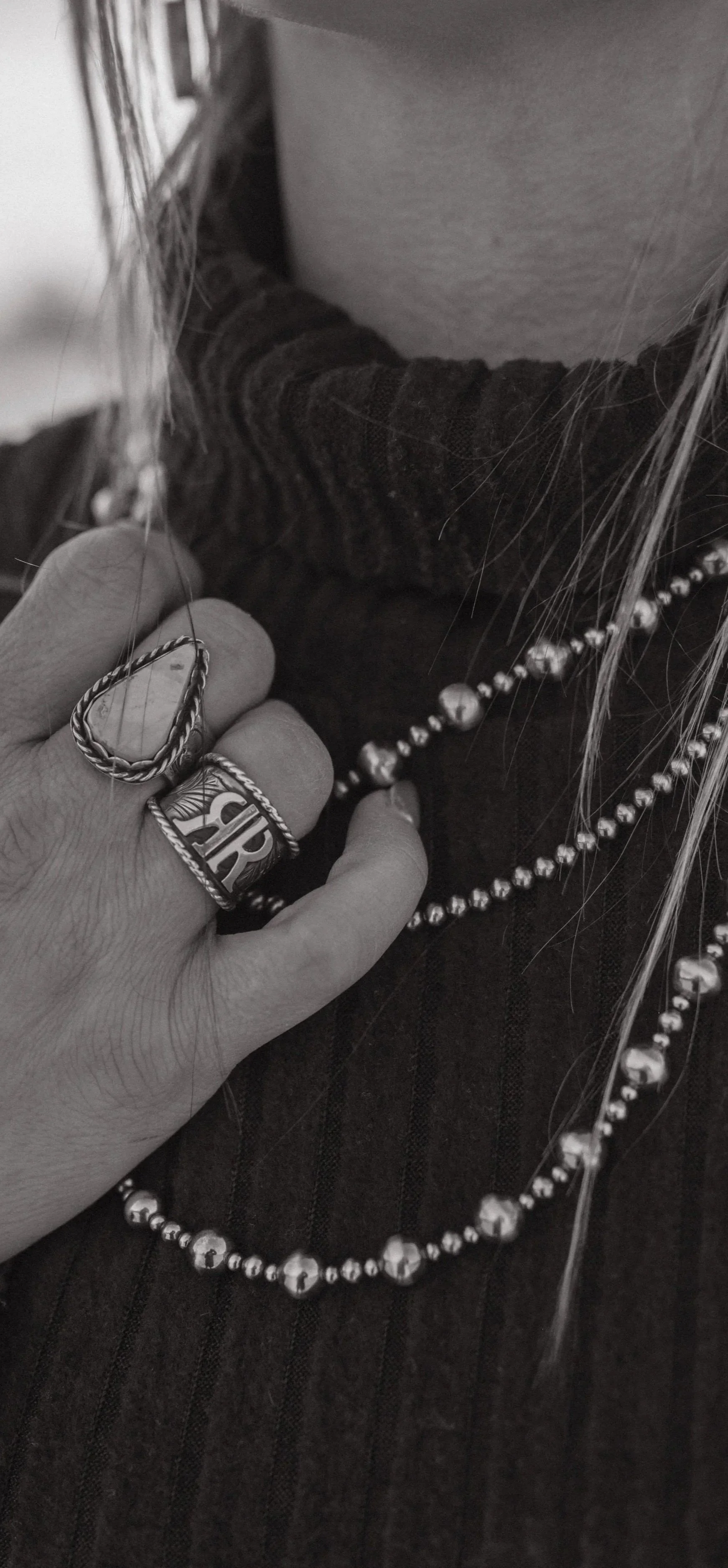 Close-up of a hand wearing rings touching a person's chest adorned with jewelry and wearing multiple necklaces.