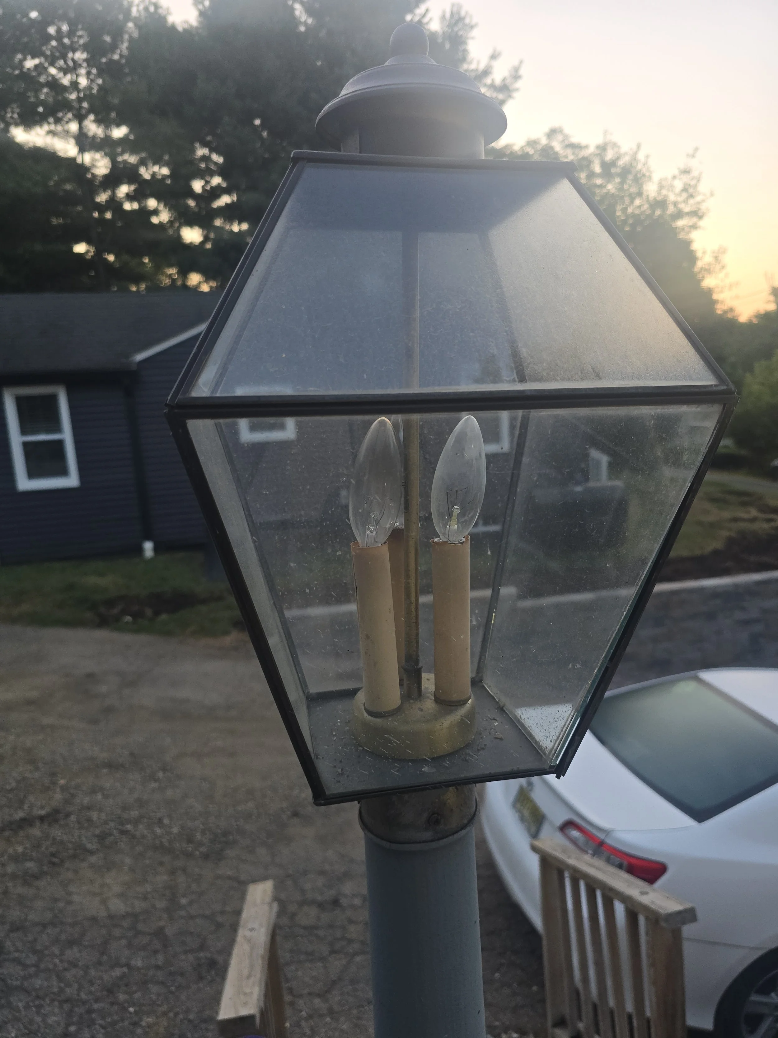 Close-up of an outdoor streetlamp with a clear glass enclosure, showing two light bulbs inside, on a cloudy evening.