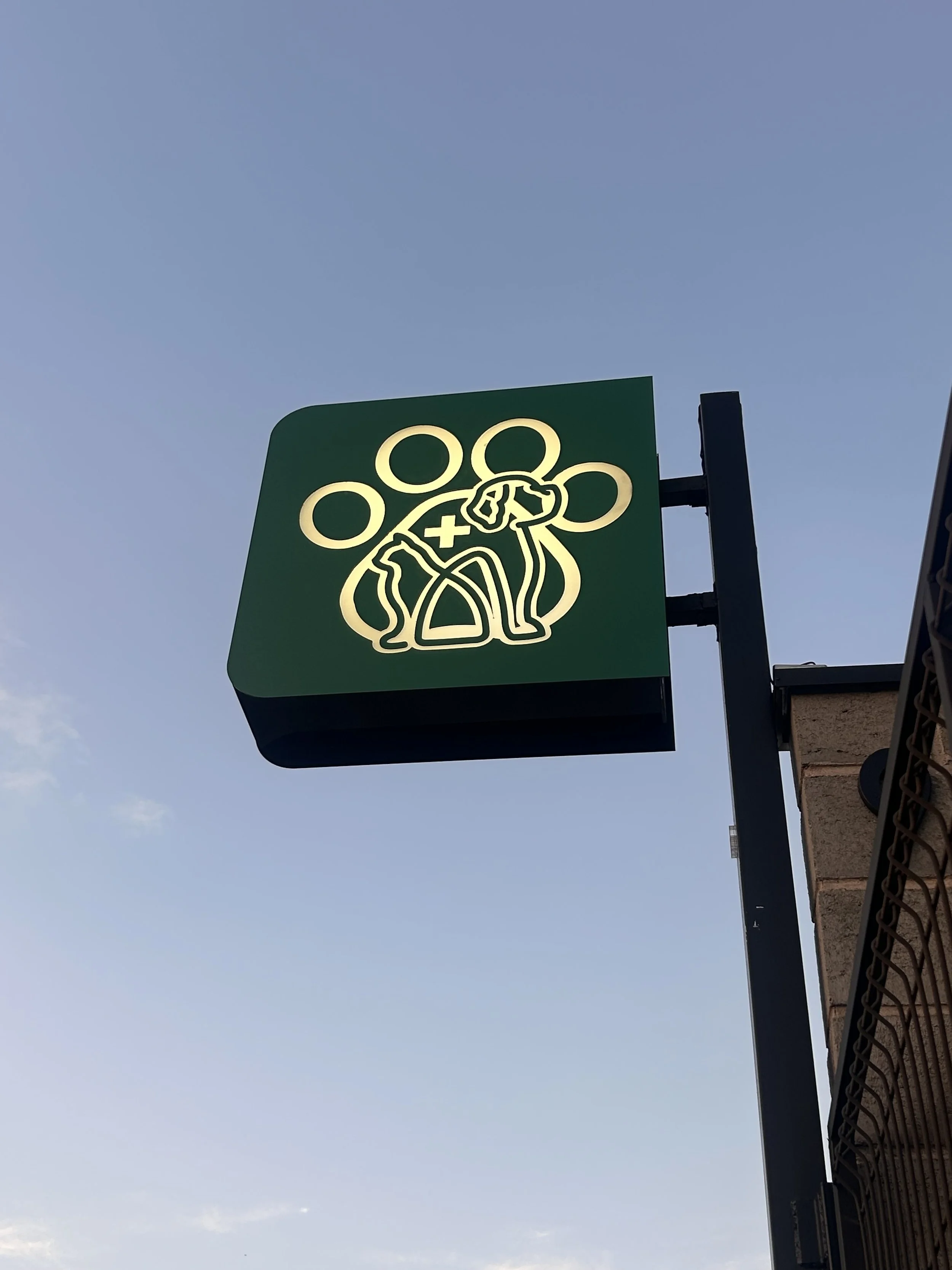 Placa com o logo estilizado do grupo de escoteiros, com círculos e uma figura de um escoteiro. Fundo verde e iluminação no logo.