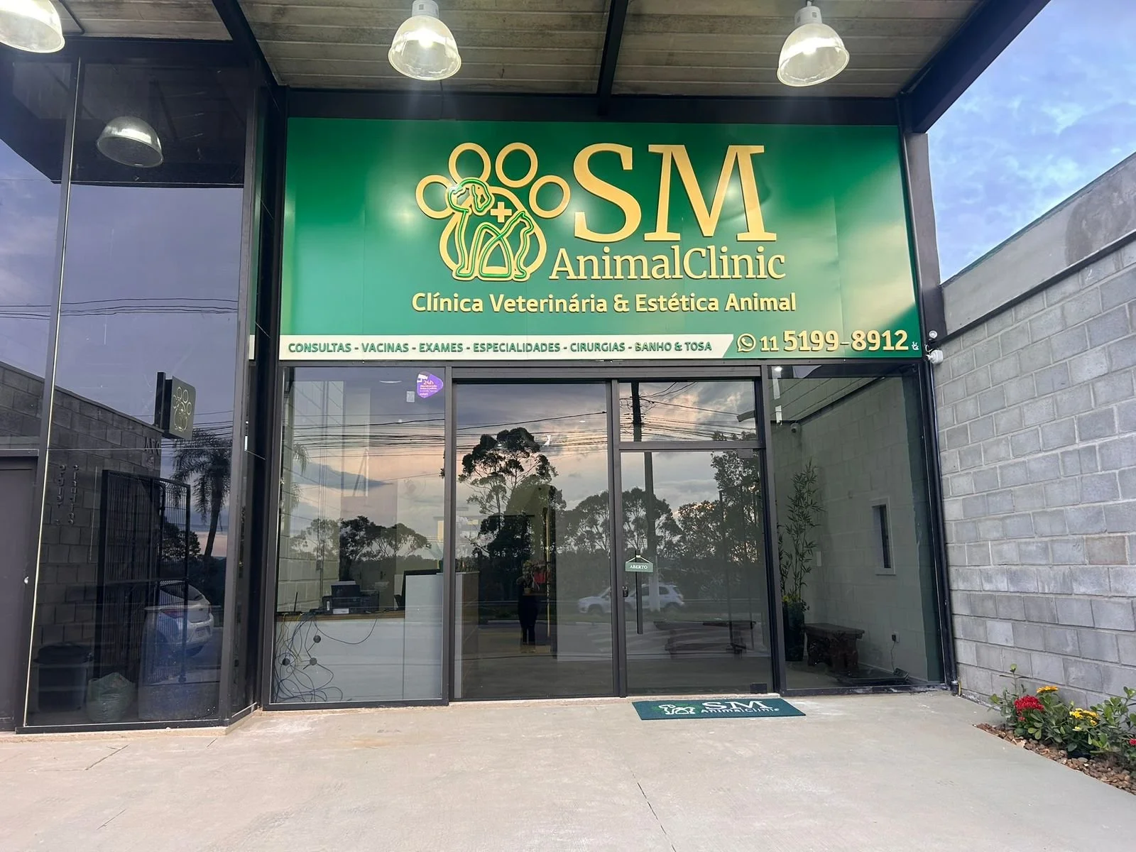 fachada de clínica veterinária chamada AnimalClinic com sinalização verde e dourada, detalhes em vidro e plantas ao redor