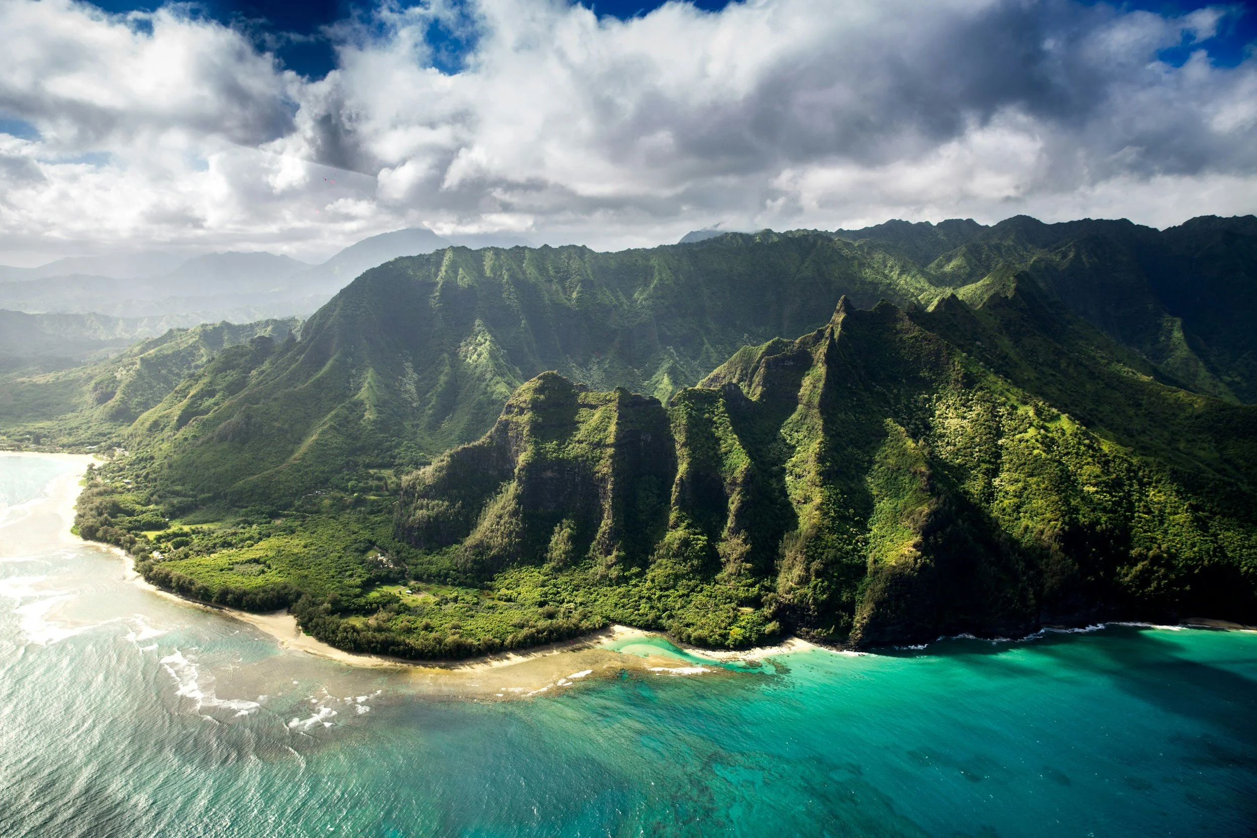 Aerial view of lush green mountains meeting turquoise ocean with sandy beach