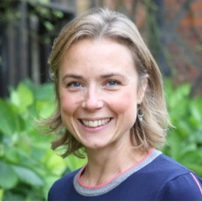 A smiling woman with shoulder-length blonde hair in an outdoor garden setting.