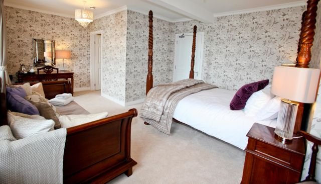 Bedroom with a four-poster bed, floral wallpaper, and a sitting area with a loveseat and side tables.