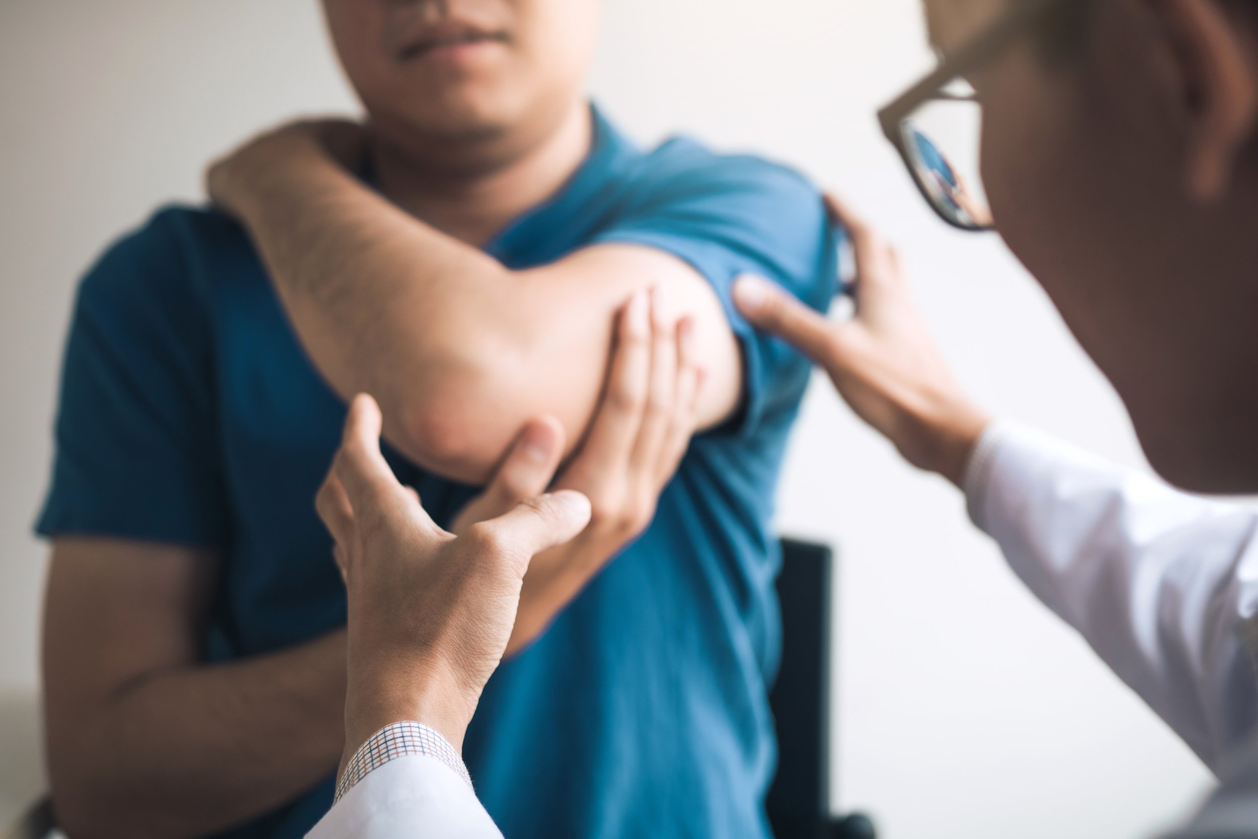 A person with a blue shirt receiving a consult for in his upper arm from a healthcare professional wearing glasses and a white coat.