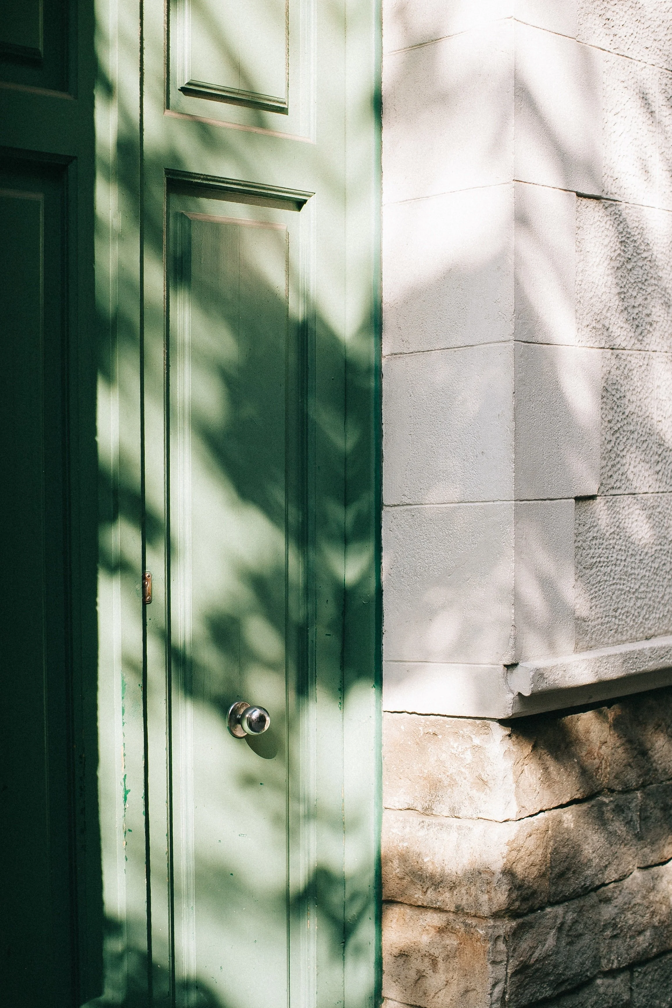 A close-up shot of a green wooden door set in a stone wall, with shadows cast across the door and wall.