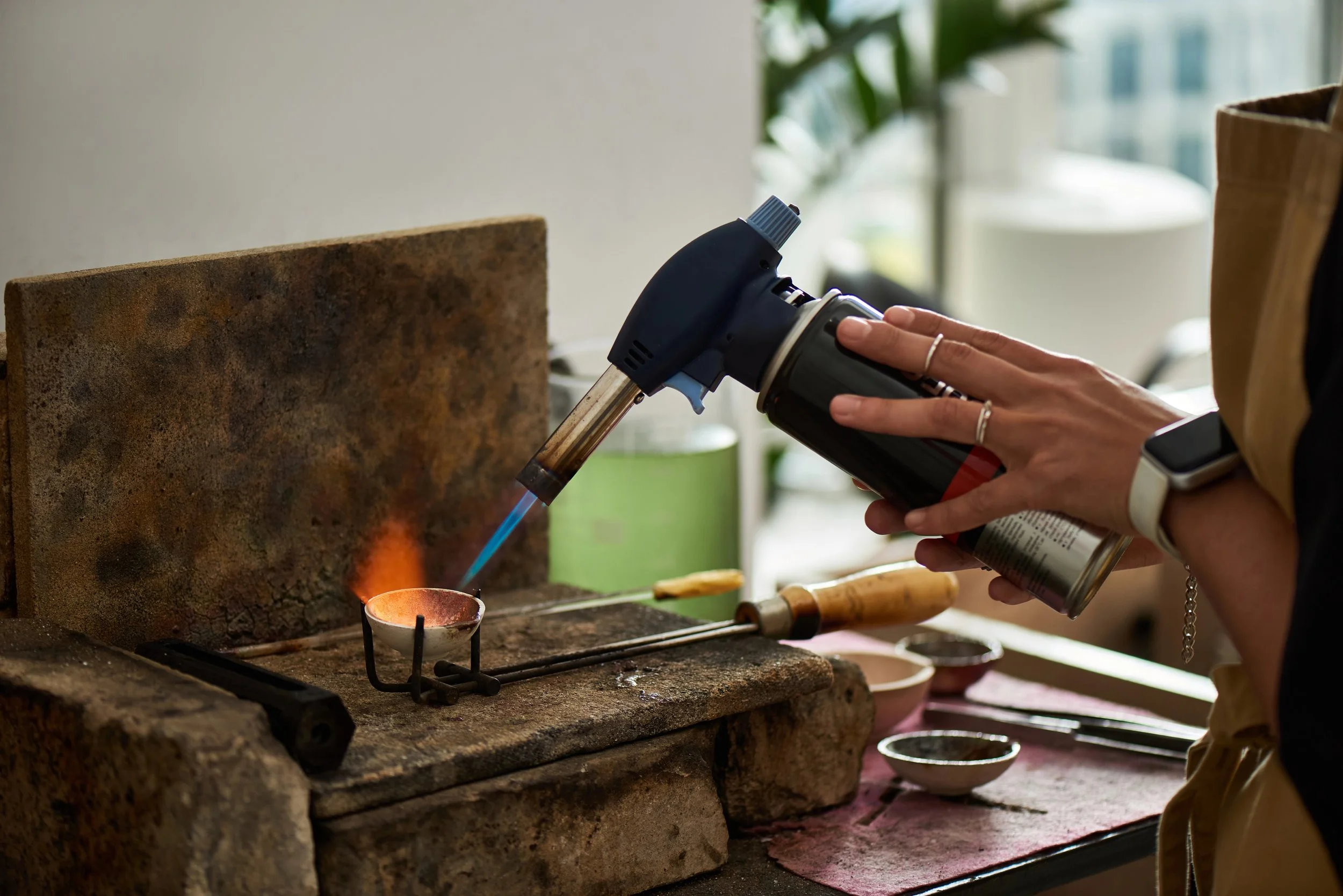 Person using a blowtorch to melt or shape metal at a workbench.