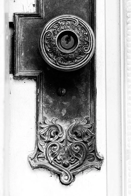 Close-up of an ornate, vintage doorbell plate with a round, decorative overlay surrounding the keyhole and a carved face and scrollwork design at the bottom.