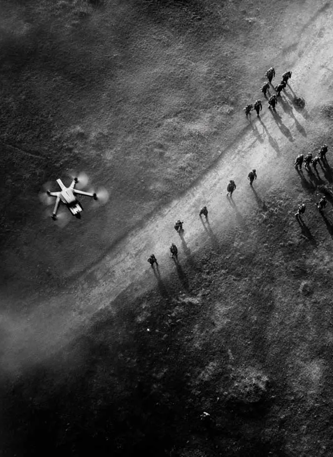Black and white aerial photograph of a group of people walking on a dirt path next to a drone lying on the ground.