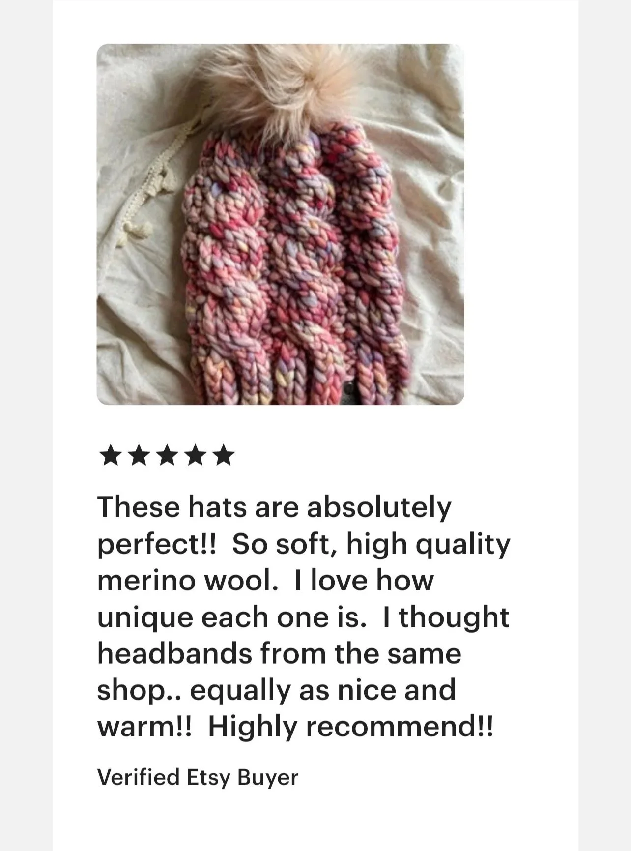 Close-up of a colorful, chunky knit wool hat with a fluffy pom-pom on top, resting on a white fabric surface.