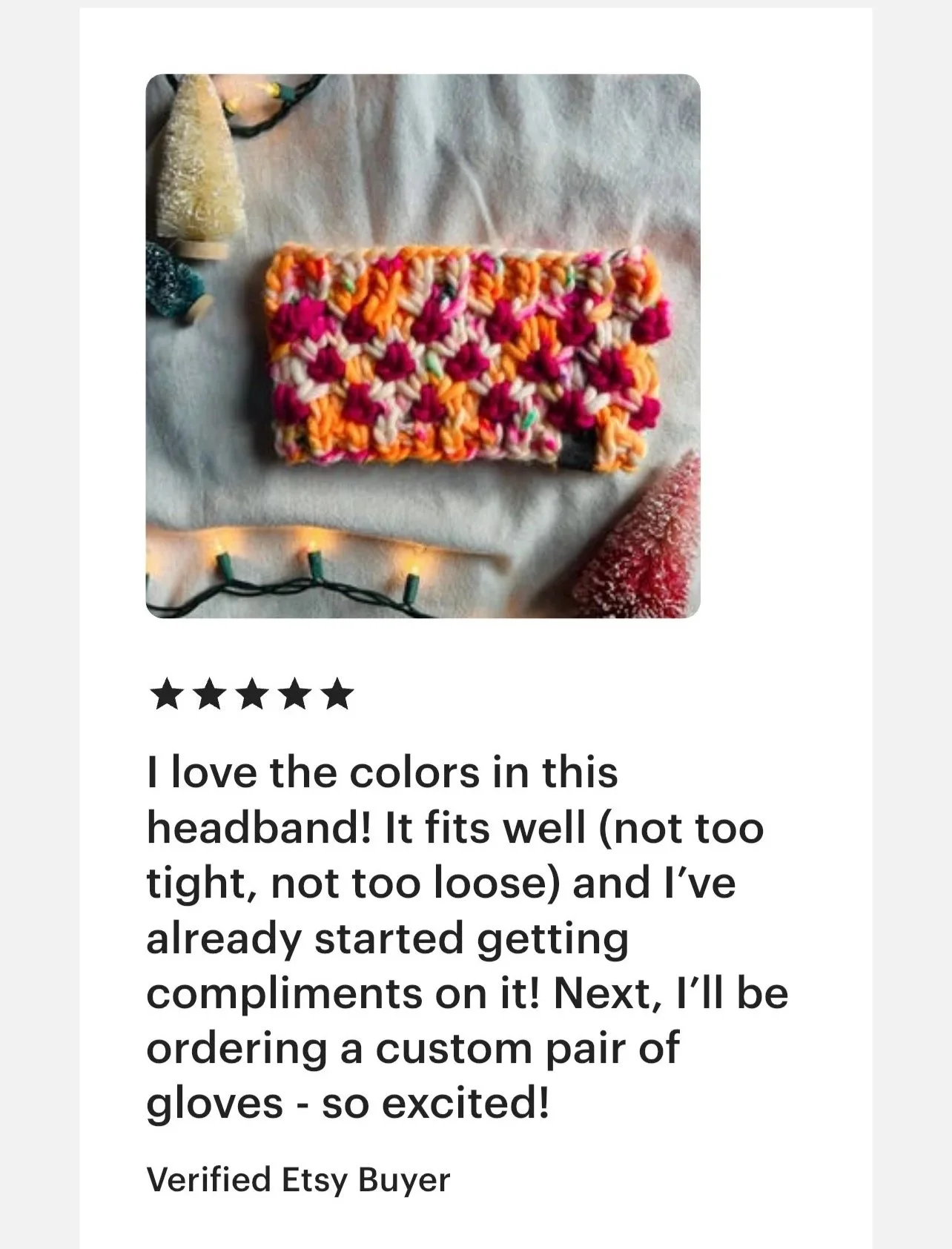 Colorful, crocheted headband with pink, orange, and cream yarn, surrounded by holiday decorations and string lights.