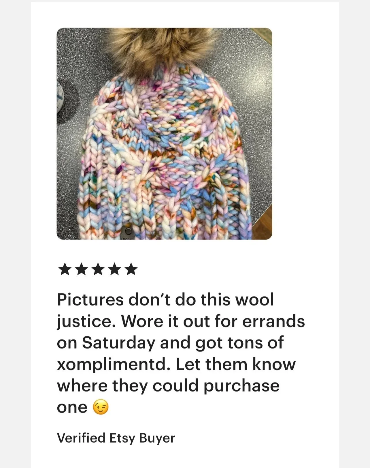Colorful, chunky knitted wool scarf with a furry hood on a speckled surface.