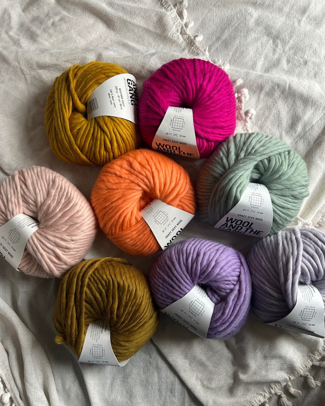 Assorted skeins of colorful yarns placed on a white fabric surface.