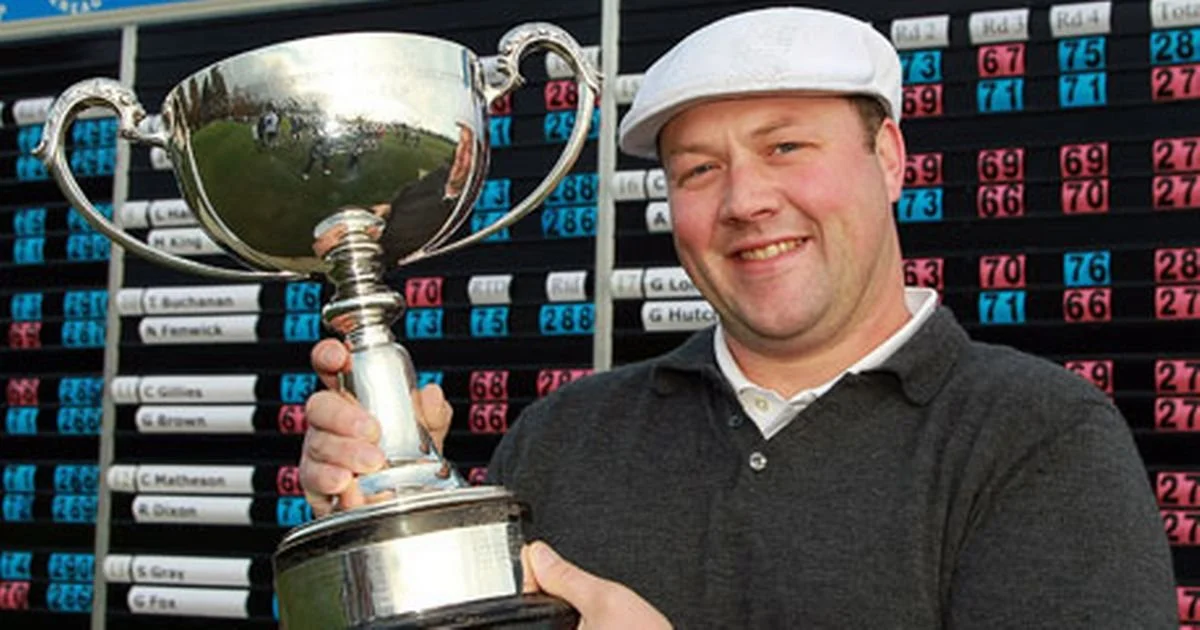 Chris Doak PGA holds a silver trophy at the Scottish PGA Championship, Gleneagles in 2010. He wears a white flat cap and smiles at the camera. He stands before a scoreboard.