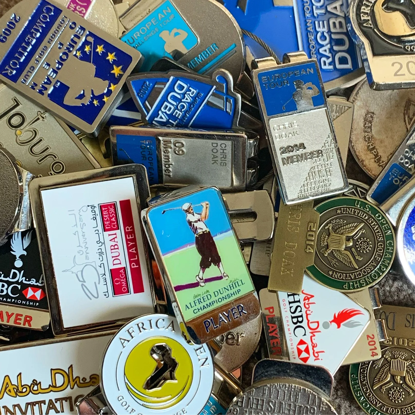 A selection of tournament belt clips and badges named Chris Doak PGA. They include: Race to Dubai; Alfred Dunhill; Abu Dhabi HSBC; US Open; European Tour; DP World Tour; African Open; Omega Dubai; Johannesburg Open