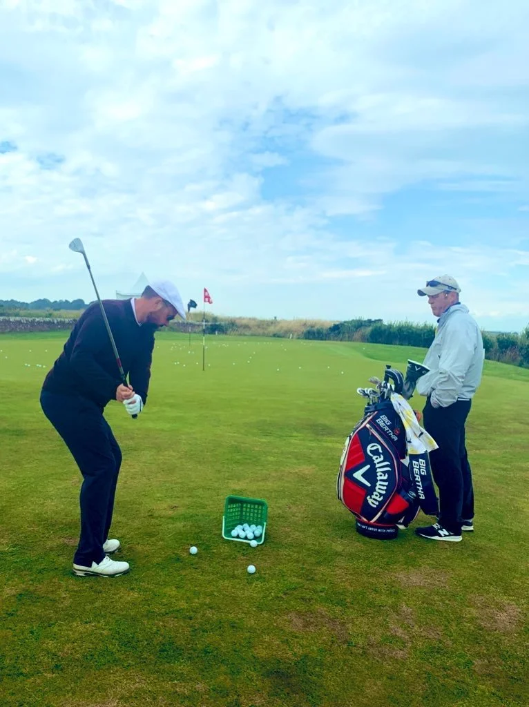 Chris Doak on the practice area at St Andrews Scotland. Chipping golf shot. His caddy watches him.