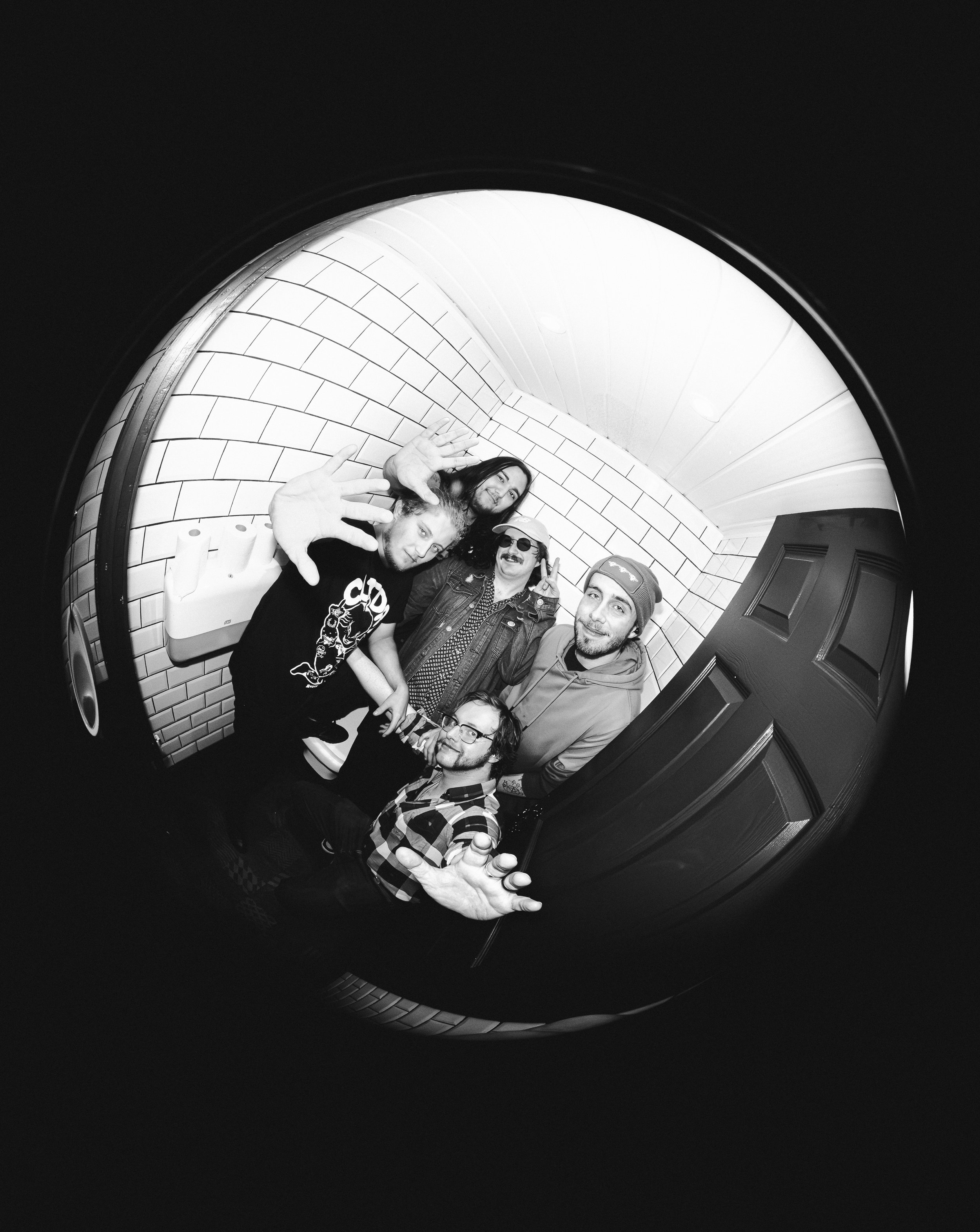 Five friends taking a group photo with a fisheye lens in black and white, showing their faces and gestures.