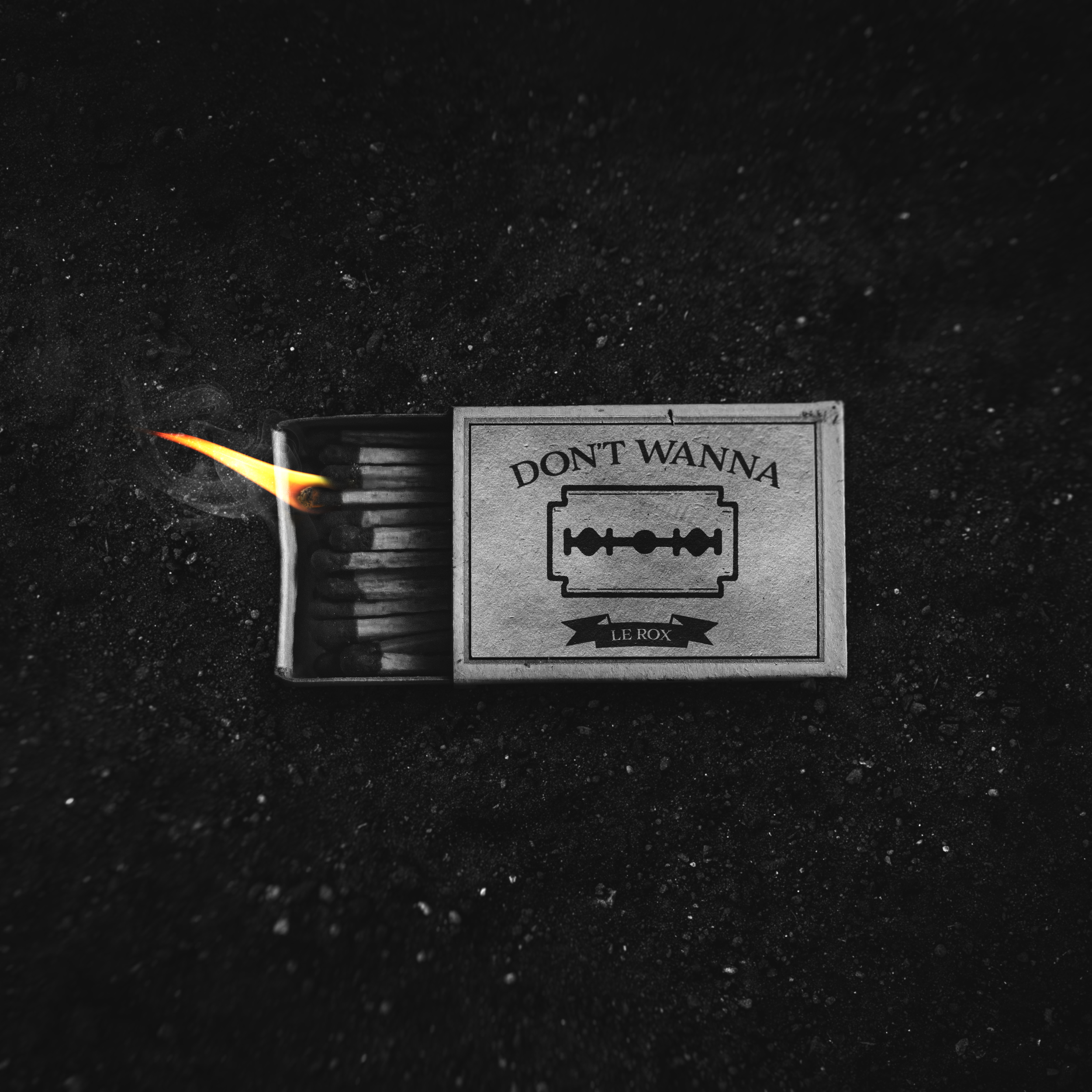 A matchstick igniting with a small flame on a dark, textured surface, partially obscured by a signage reading 'DON'T WANA' with an razor blade and the logo 'LE ROX'.