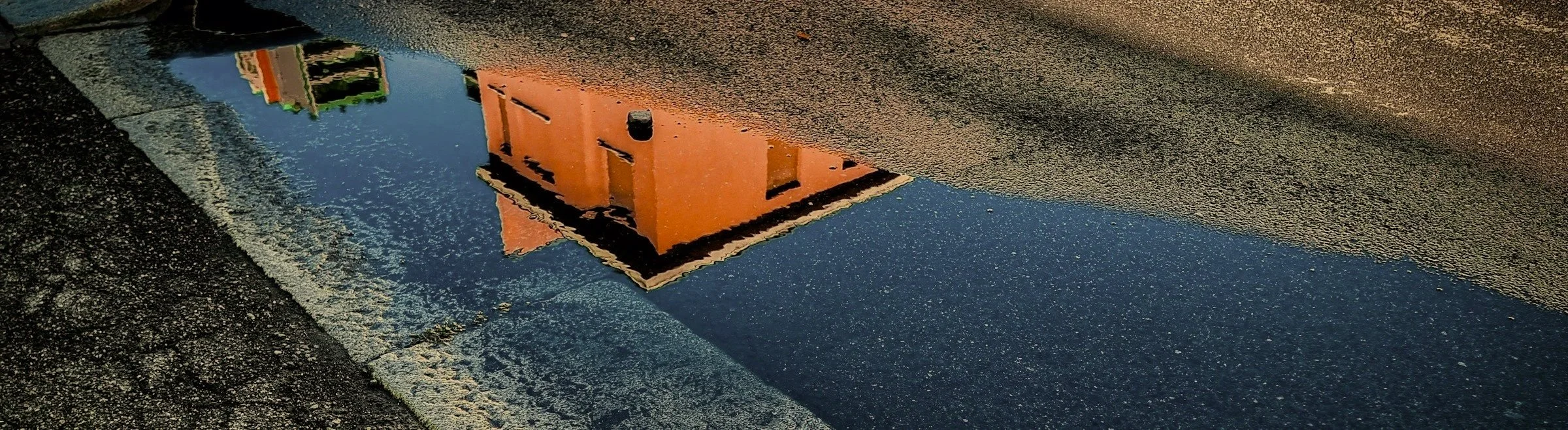 Reflection of an orange building in a puddle on the street.
