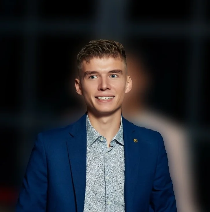 Jeune homme souriant en costume bleu, arrière-plan flou.