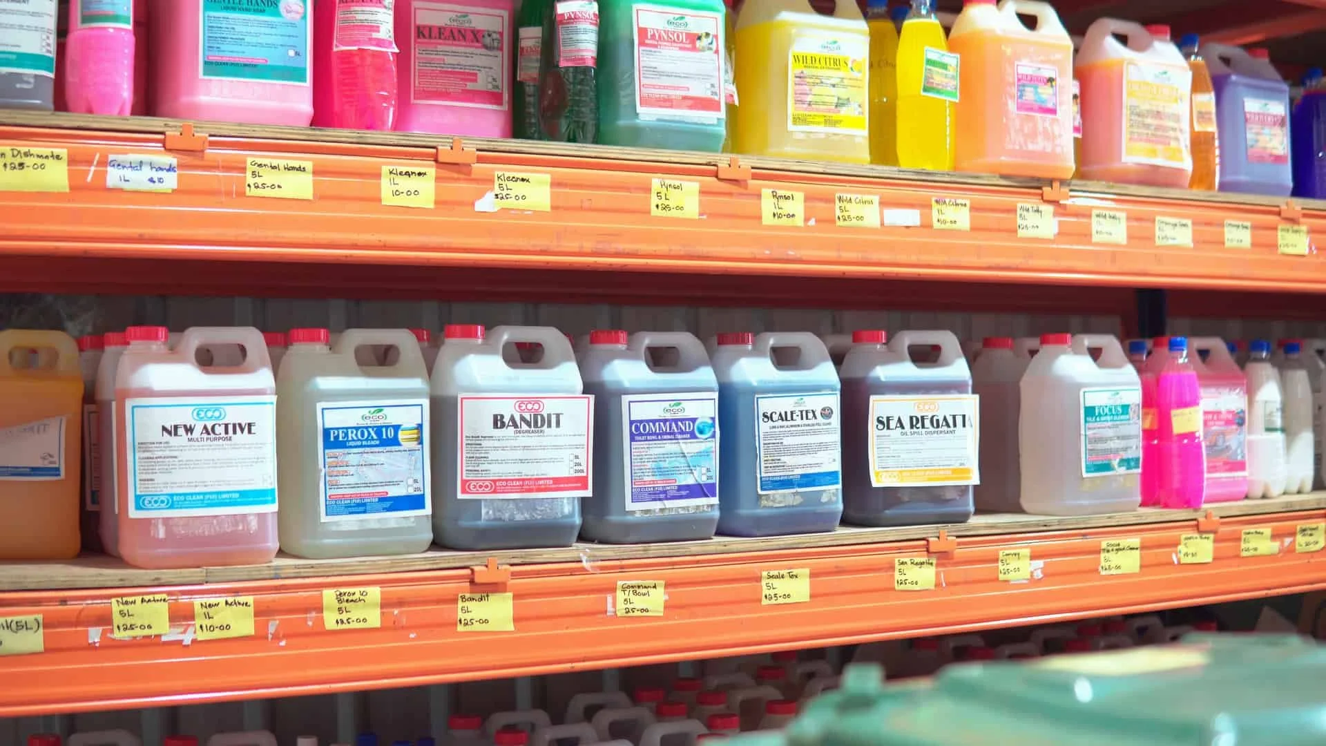 A woman and a warehouse worker walking and talking in a warehouse aisle, with shelves filled with packages and supplies in the background.