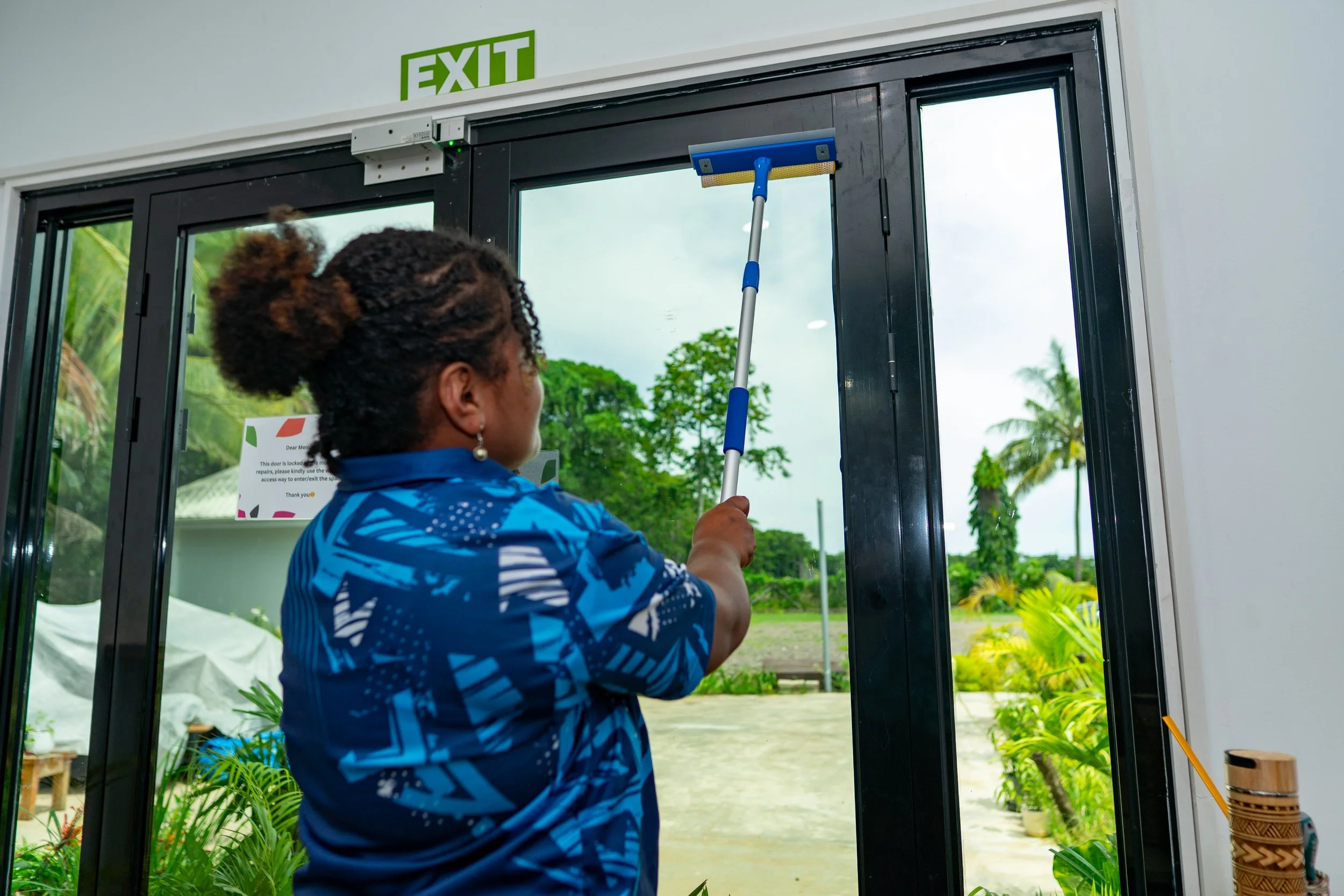 Person wearing black clothing holds a yellow spray bottle, spraying a fine mist of disinfectant or cleaning solution onto a dark surface.