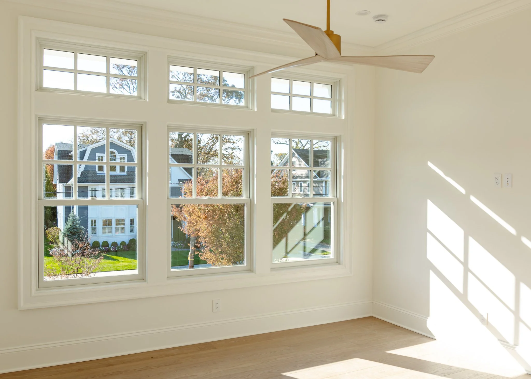 Habitación luminosa con ventanas grandes, suelo de madera clara y ventilador de techo de diseño moderno