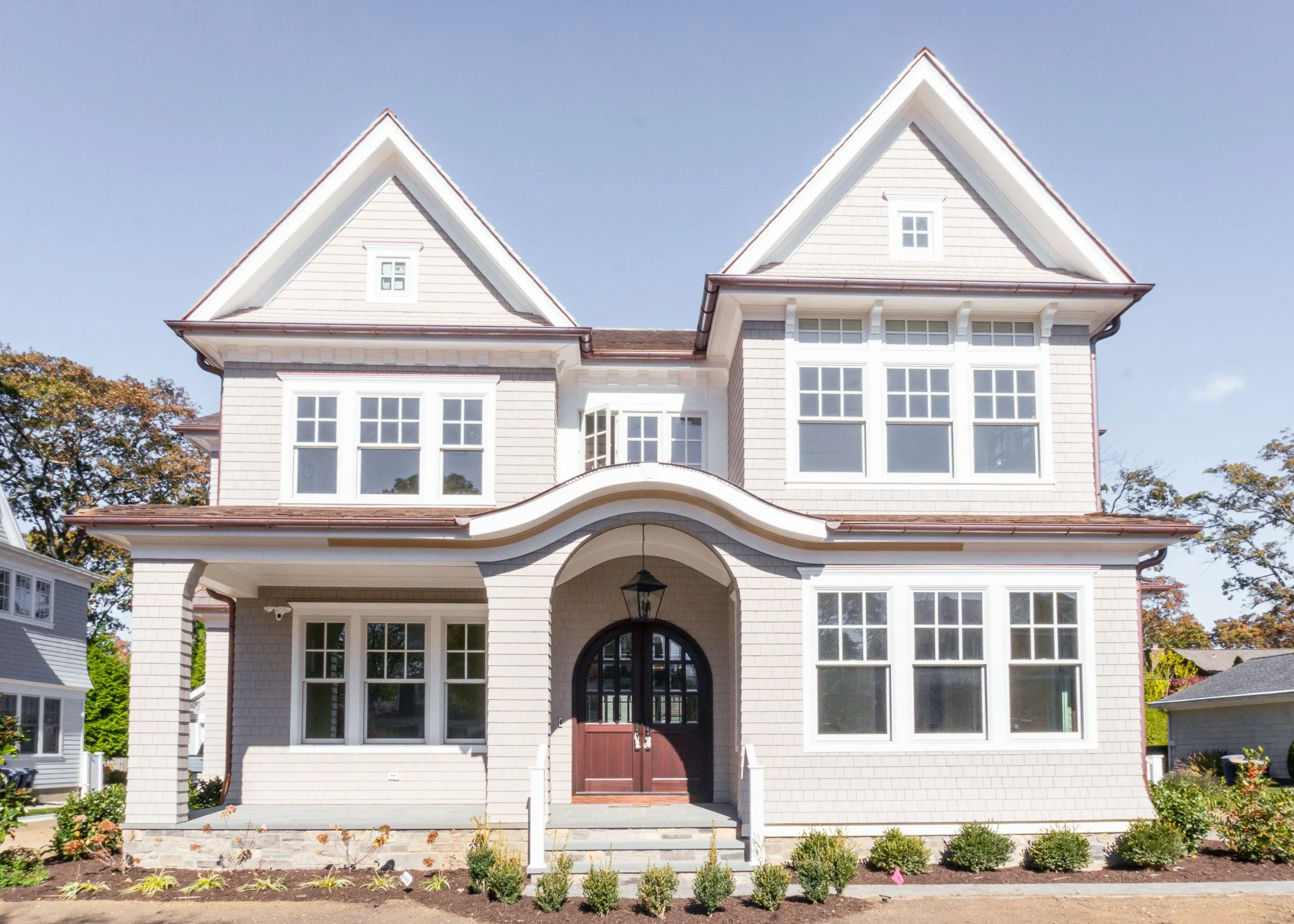 Casa grande de estilo clásico con ventanas grandes y jardín con plantas en el frente, en un día soleado.