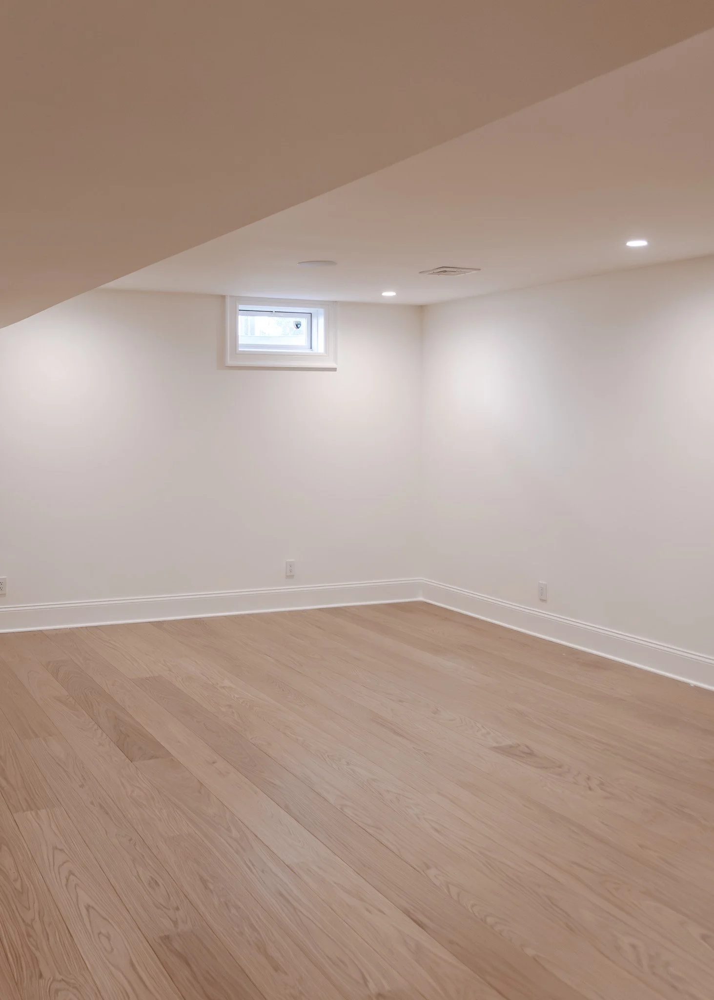 Espacio vacío con paredes blancas, suelo de madera clara y una pequeña ventana.