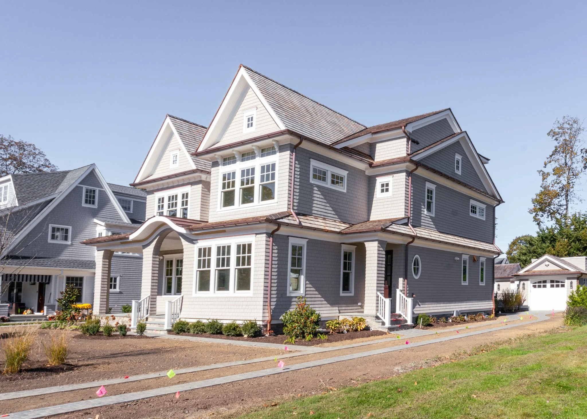 Casa grande de estilo residencial con varias ventanas, pintura gris y tejado de tejas, rodeada de un jardín en proceso de jardinería.