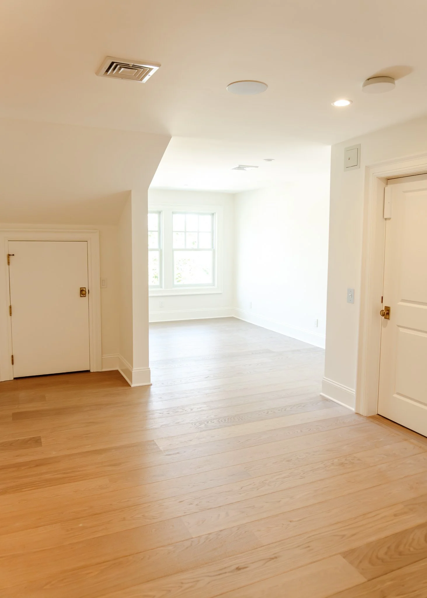 Interiores de una casa con paredes blancas, pisos de madera clara y ventanas grandes que dejan entrar luz natural.