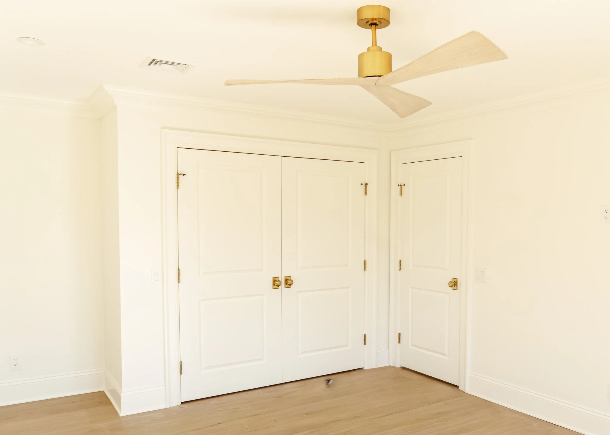 Habitación con puertas blancas, techo con ventilador de palas beige y suelo de madera claro.