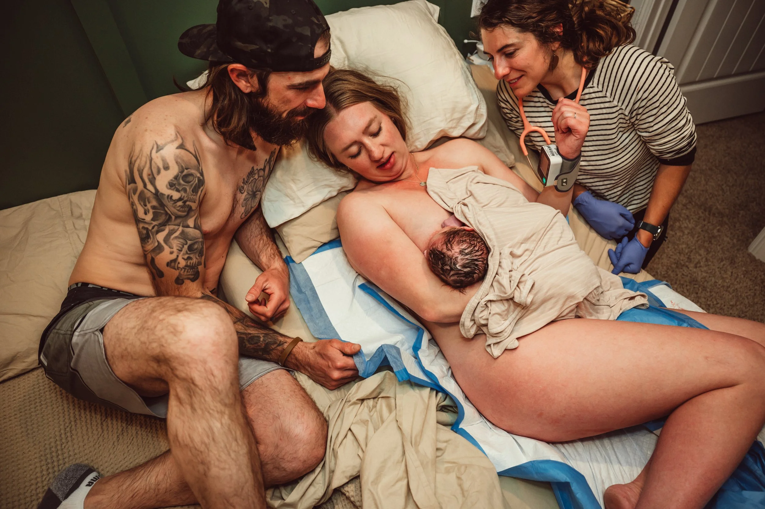 A woman giving birth in a bed with a man and a healthcare professional nearby.