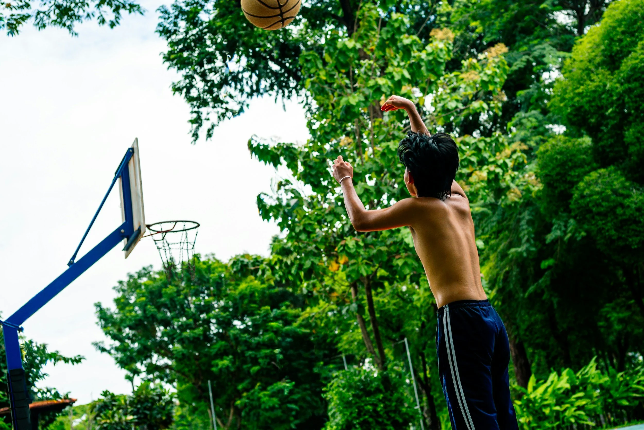 Child shooting a basketball into a hoop in a wooded park